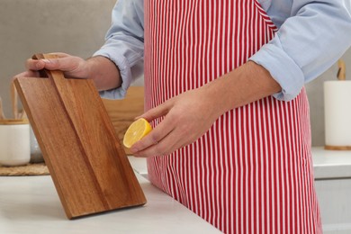 Photo of Man with wooden cutting board and lemon at light table in kitchen, closeup