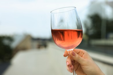 Photo of Woman holding glass of rose wine outdoors, closeup. Space for text