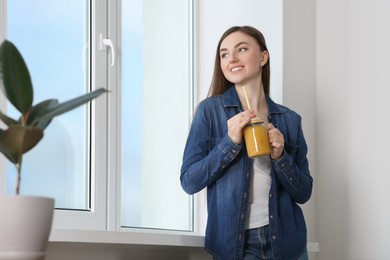 Photo of Beautiful young woman with delicious smoothie near window at home