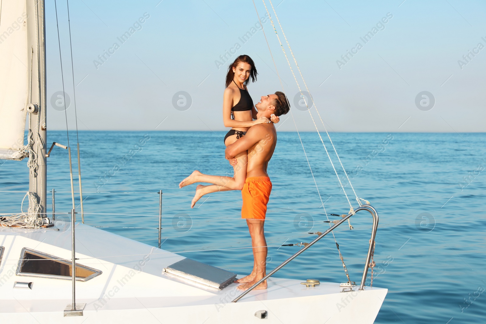 Photo of Young man and his beautiful girlfriend in bikini on yacht. Happy couple during sea trip