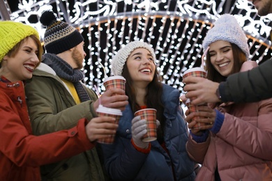 Photo of Happy friends with cups of mulled wine at winter fair