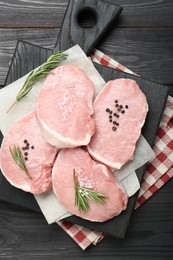 Photo of Pieces of raw pork meat and spices on black wooden table, top view