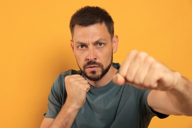 Aggressive man throwing punch on orange background
