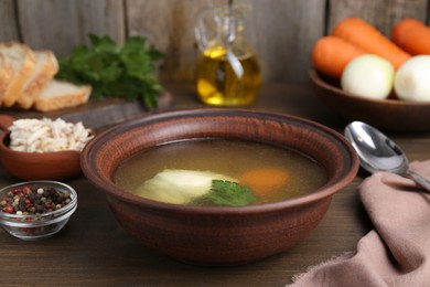 Delicious chicken bouillon with carrot and parsley in bowl on wooden table, closeup