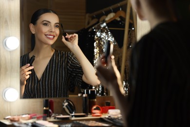Photo of Bright makeup. Beautiful woman applying mascara near mirror in dressing room