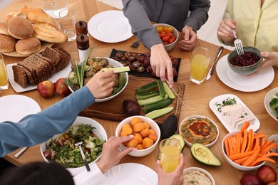 Photo of Friends eating vegetarian food at wooden table indoors, closeup