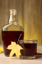 Tasty maple syrup and leaf on wooden table