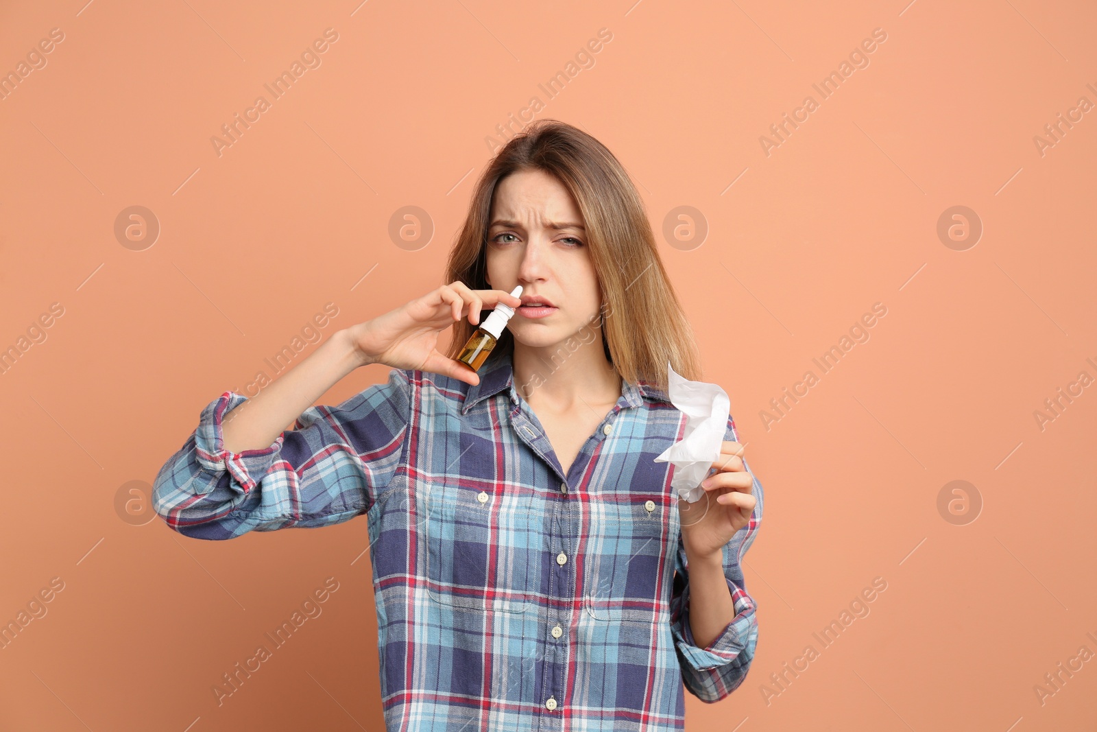 Photo of Sick young woman using nasal spray on coral background