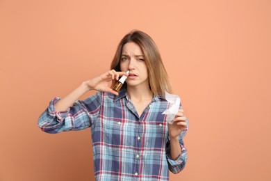 Sick young woman using nasal spray on coral background