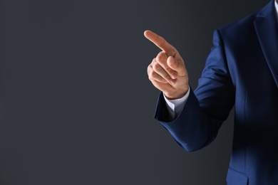 Photo of Businessman touching empty virtual screen against dark background, focus on hand