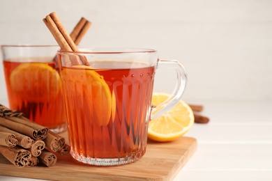 Delicious hot tea with cinnamon and lemon on white wooden table, closeup. Space for text