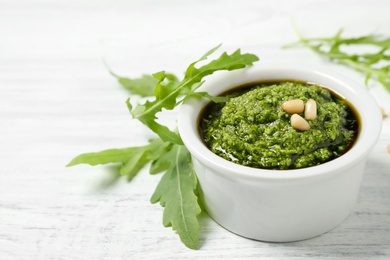 Bowl of tasty pesto and arugula on white wooden table