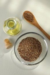 Photo of Caraway (Persian cumin) seeds and essential oil on white table, flat lay