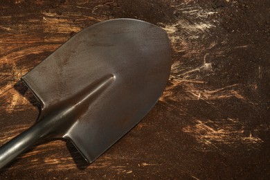 Photo of Metal shovel with fertile soil on dirty wooden surface, top view. Space for text