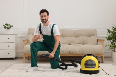 Photo of Dry cleaner's employee hoovering carpet with vacuum cleaner and showing thumbs up in room