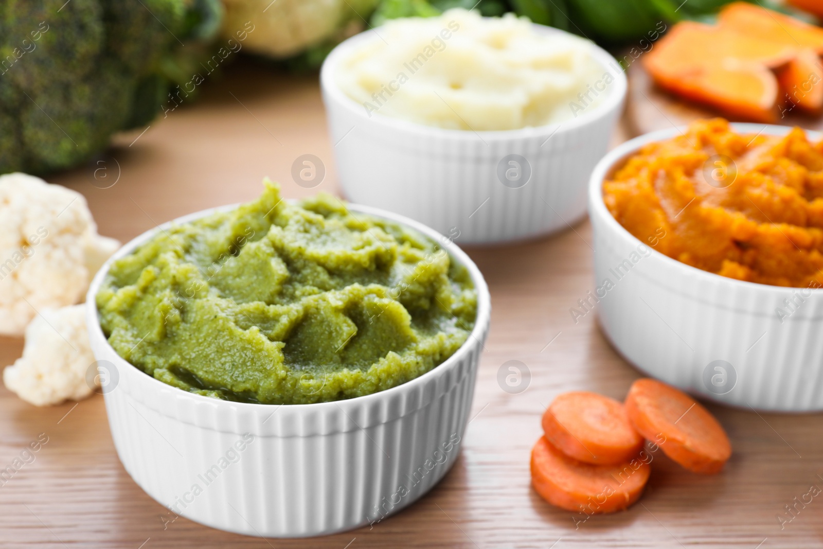 Photo of Bowls with tasty puree and ingredients on wooden table, closeup