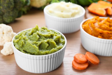 Bowls with tasty puree and ingredients on wooden table, closeup