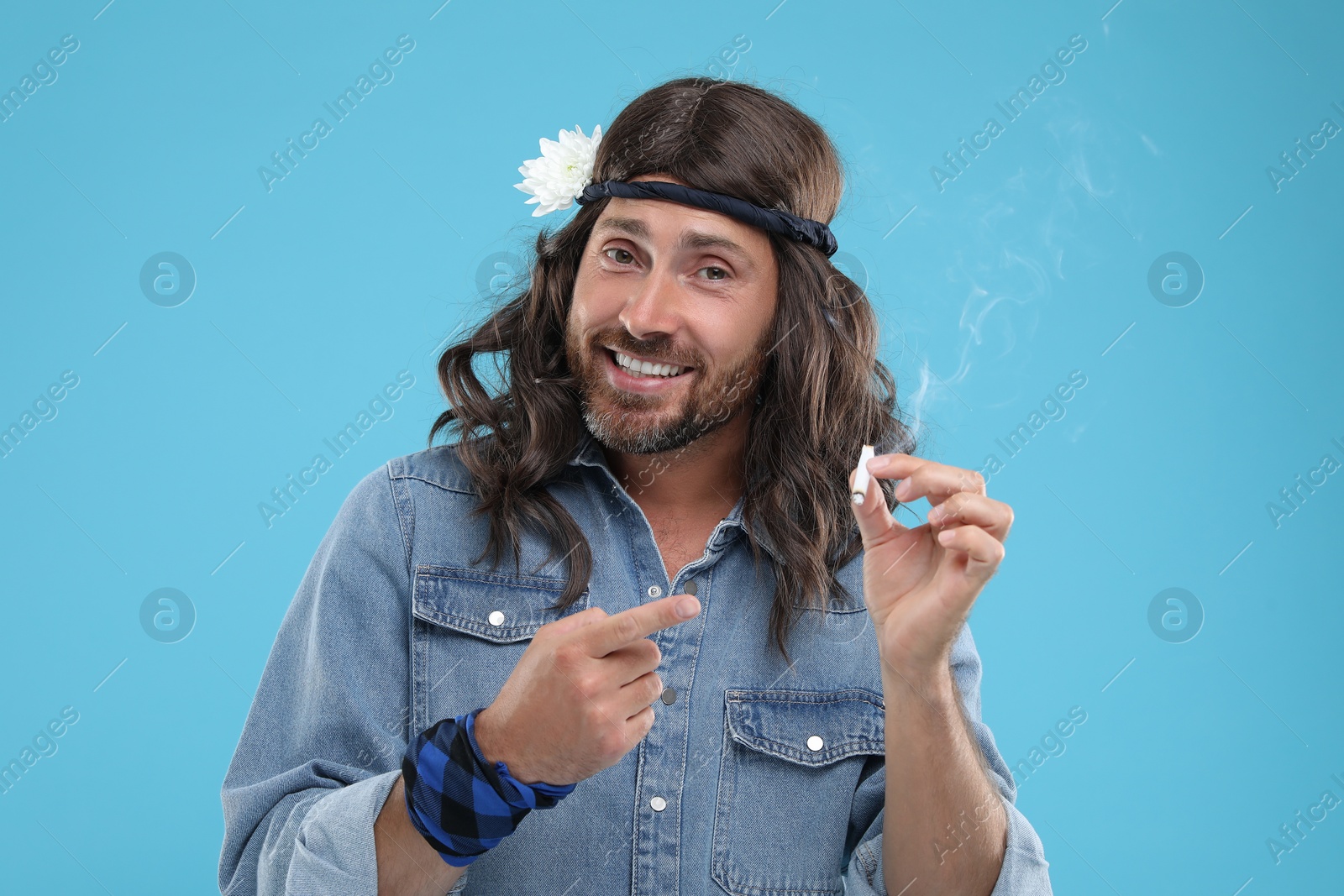 Photo of Stylish hippie man pointing at cigarette on light blue background