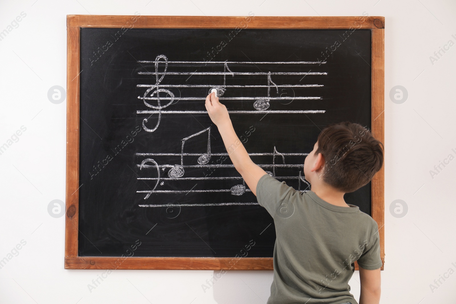 Photo of Little boy writing music notes on blackboard in classroom