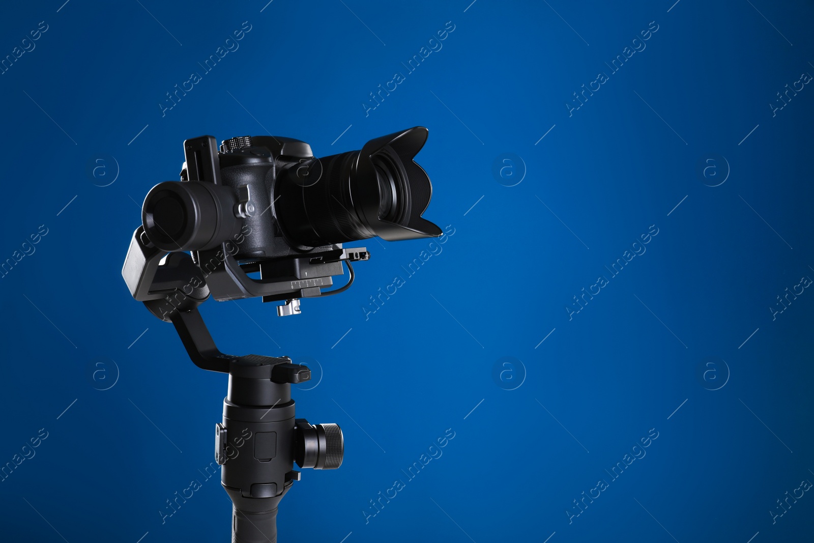 Photo of Modern professional video camera on blue background. Space for text
