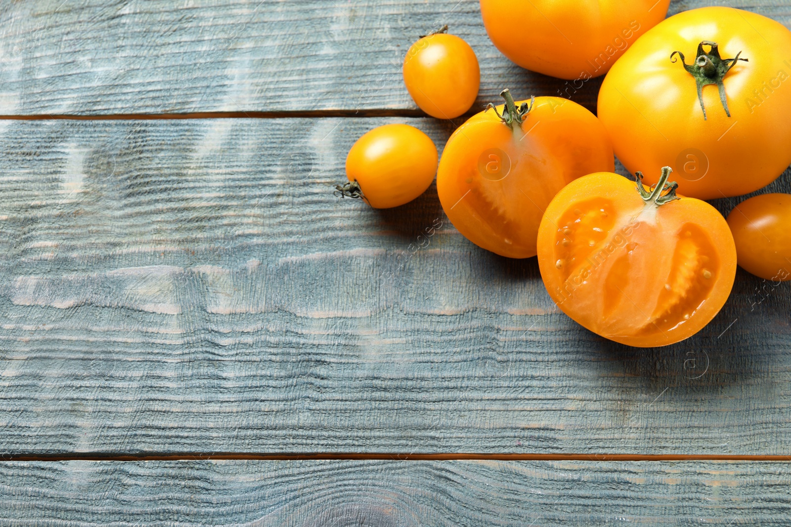 Photo of Fresh ripe yellow tomatoes on light blue wooden table, above view. Space for text