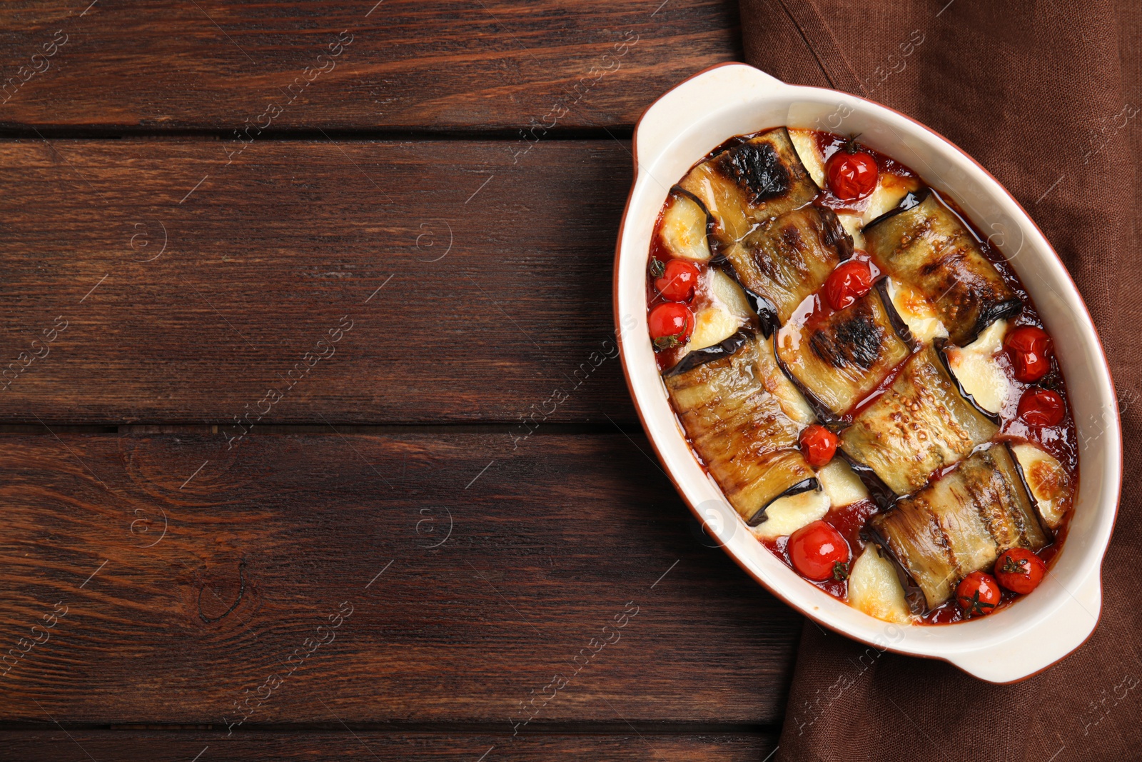 Photo of Tasty eggplant rolls with tomatoes and cheese in baking dish on wooden table, top view. Space for text