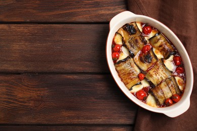 Photo of Tasty eggplant rolls with tomatoes and cheese in baking dish on wooden table, top view. Space for text