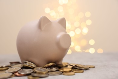 Photo of Piggy bank and coins on grey table against blurred lights