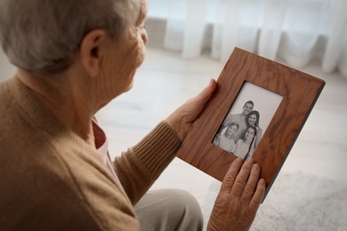 Photo of Elderly woman with framed family portrait at home