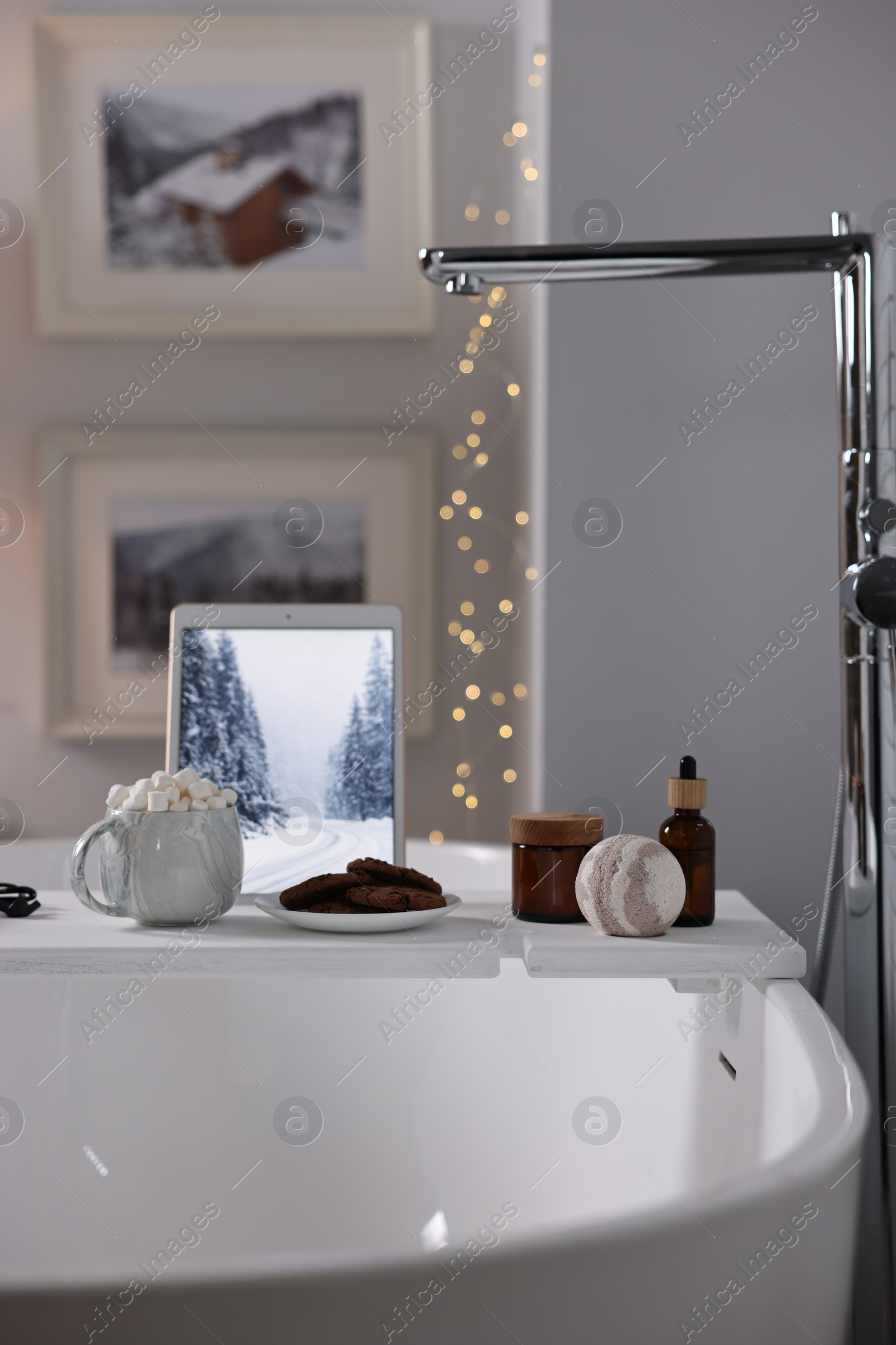 Photo of White wooden tray with tablet and spa products on bathtub in bathroom