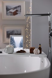 White wooden tray with tablet and spa products on bathtub in bathroom