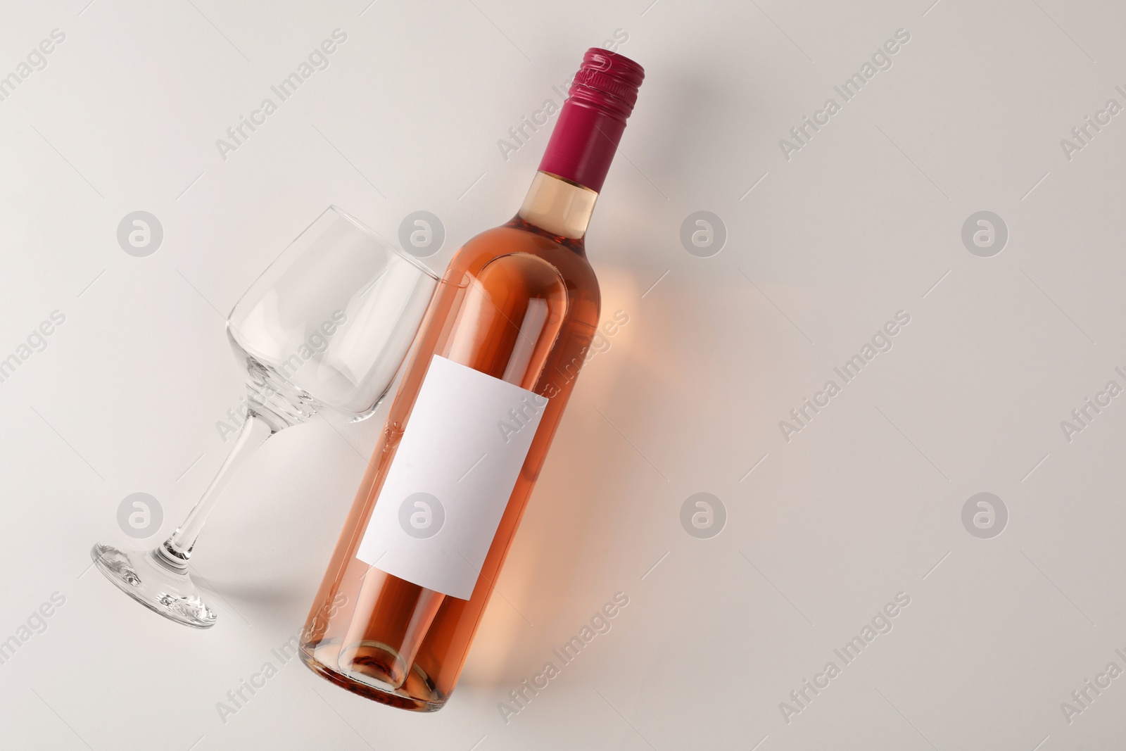 Photo of Bottle of tasty rose wine and glass on white background, flat lay. Space for text