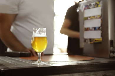 Photo of Cold tasty light beer on table in crowded bar. Space for text