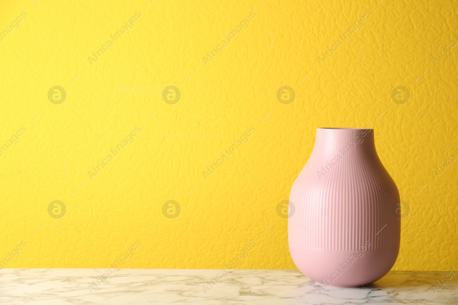 Photo of Stylish pink ceramic vase on white marble table against yellow background. Space for text