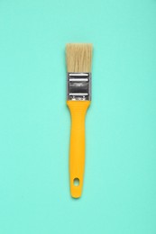 Photo of One paint brush with yellow handle on turquoise background, top view