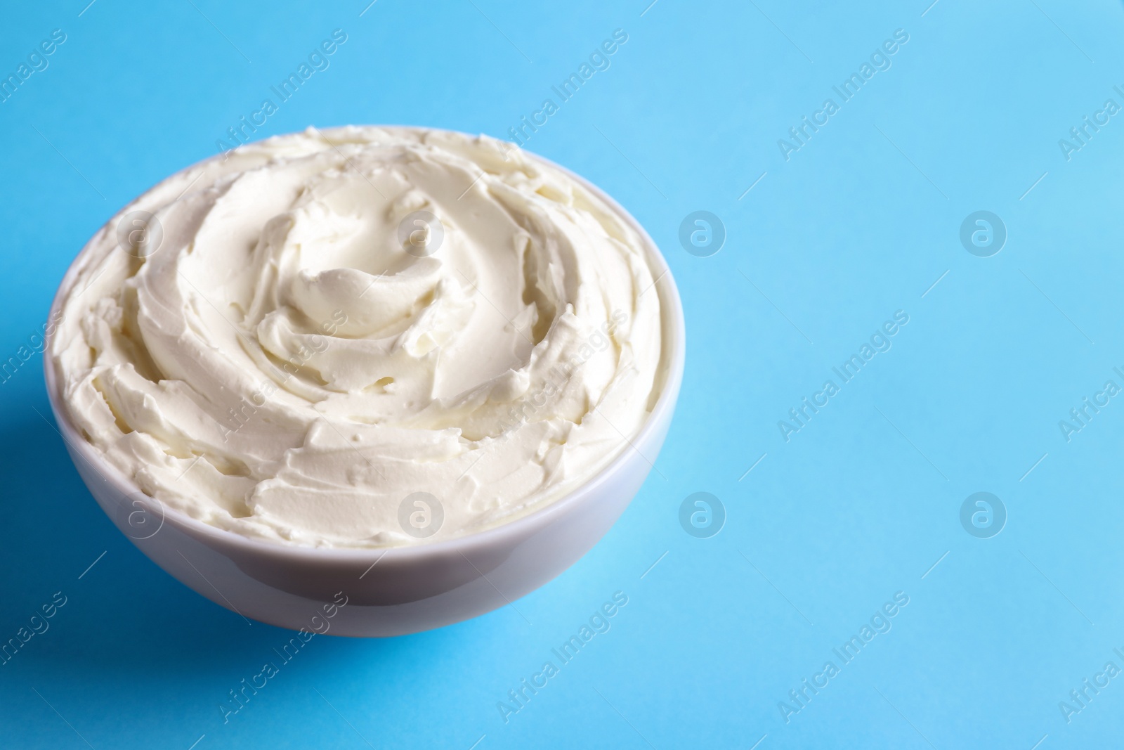 Photo of Bowl of tasty cream cheese on light blue background, space for text