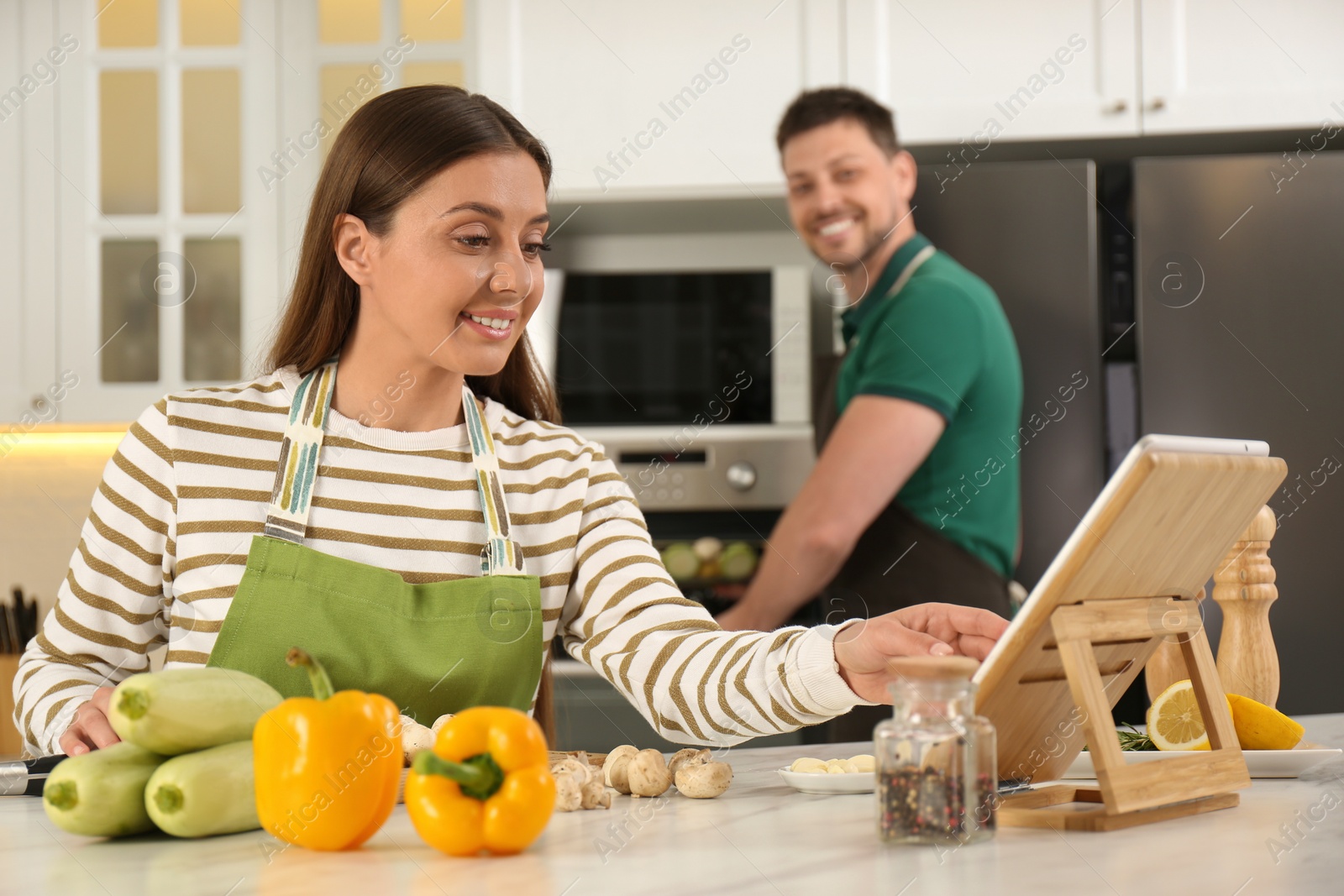 Photo of Couple making dinner together while watching online cooking course via tablet in kitchen