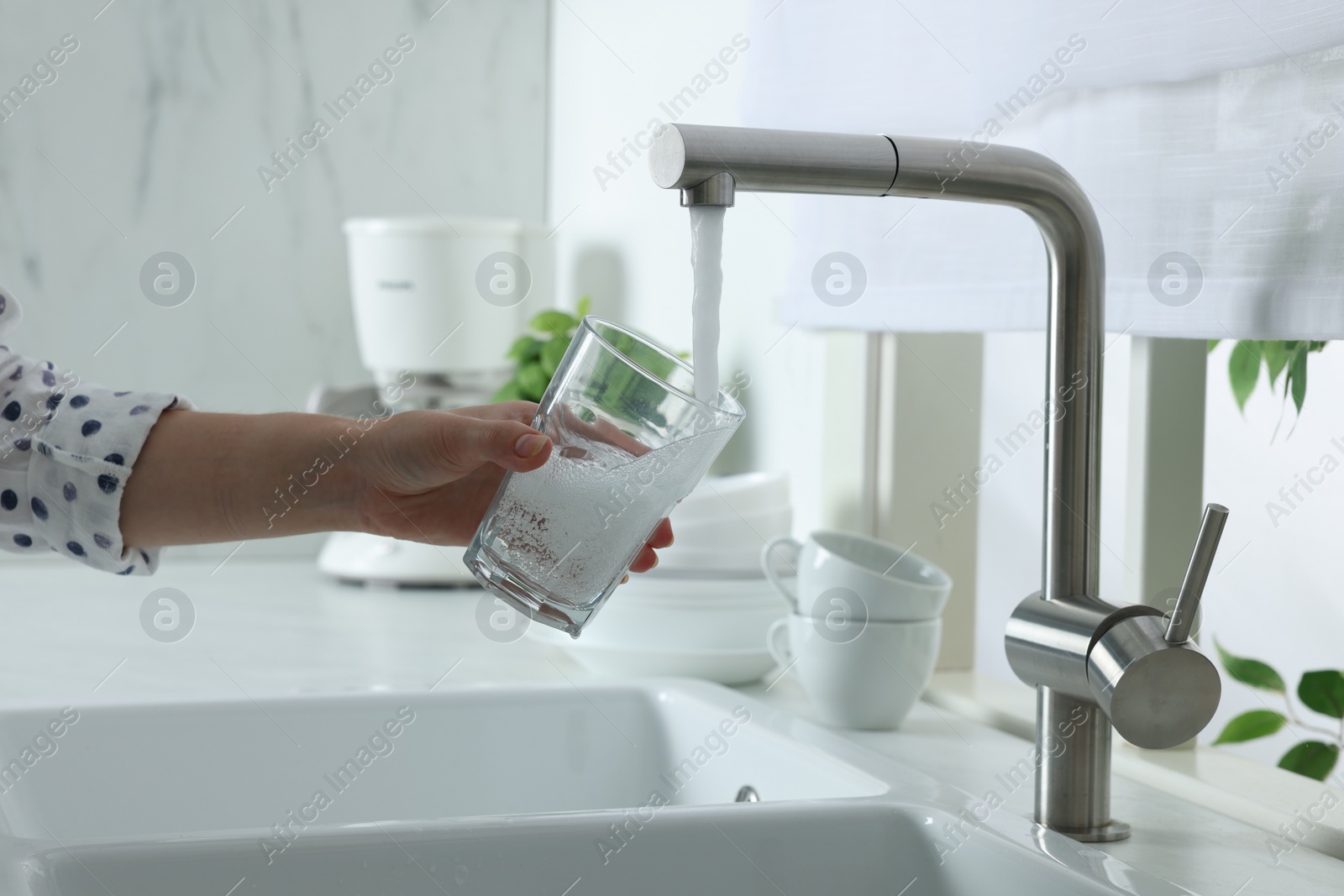 Photo of Woman filling glass with water from tap in kitchen, closeup