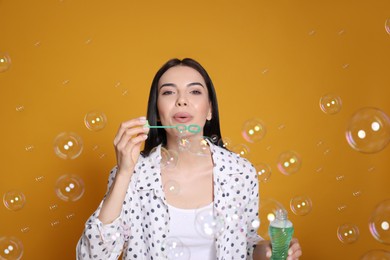 Young woman blowing soap bubbles on yellow background