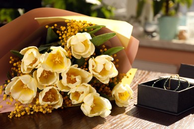 Photo of Bouquet with beautiful tulips, mimosa flowers and box of jewelry on wooden table indoors