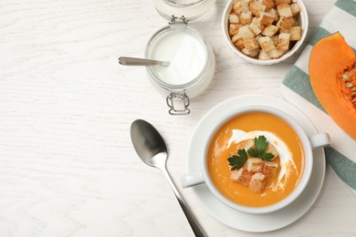 Delicious pumpkin soup in bowl served on white wooden table, flat lay. Space for text
