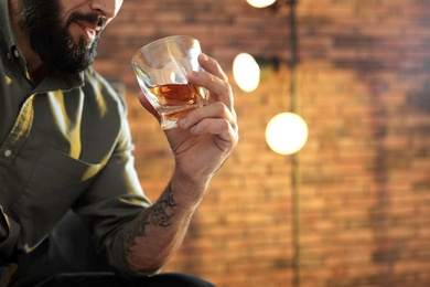Man with glass of whiskey indoors, closeup. Space for text