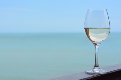 Photo of Glass with wine on railing near sea. Space for text