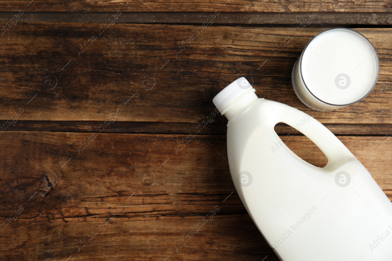 Photo of Gallon bottle and glass of milk on wooden table, flat lay. Space for text