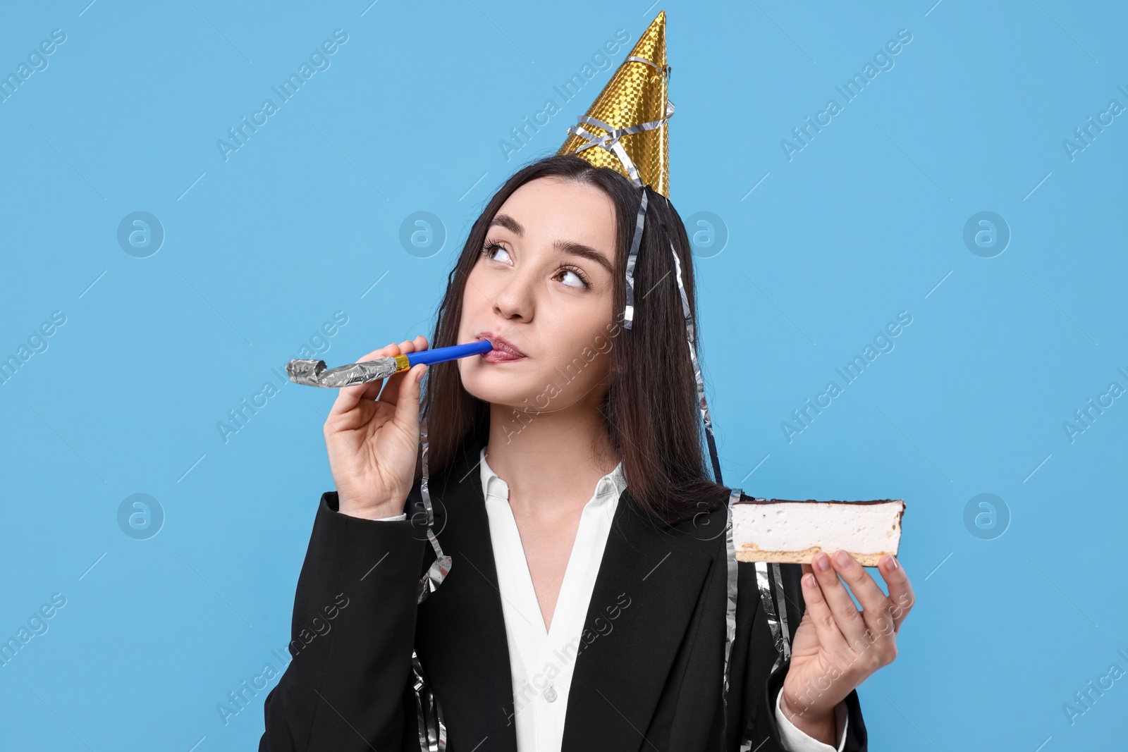 Photo of Woman in party hat with blower and piece of tasty cake on light blue background