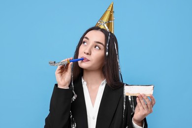 Woman in party hat with blower and piece of tasty cake on light blue background