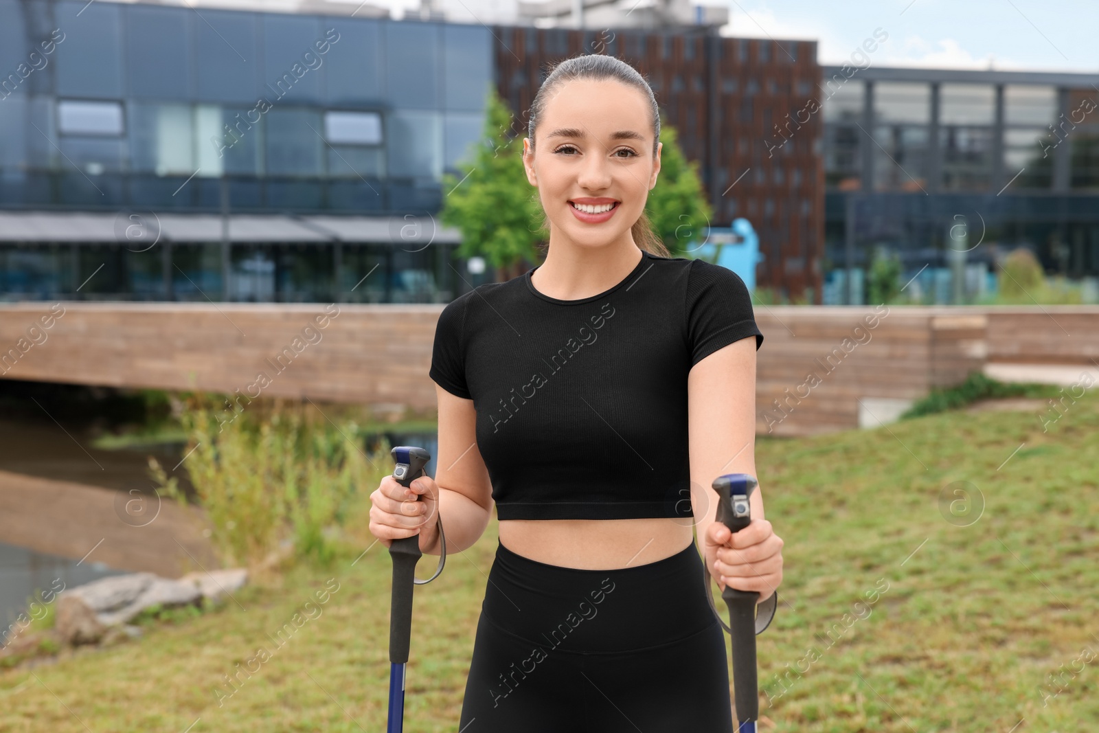 Photo of Young woman practicing Nordic walking with poles outdoors