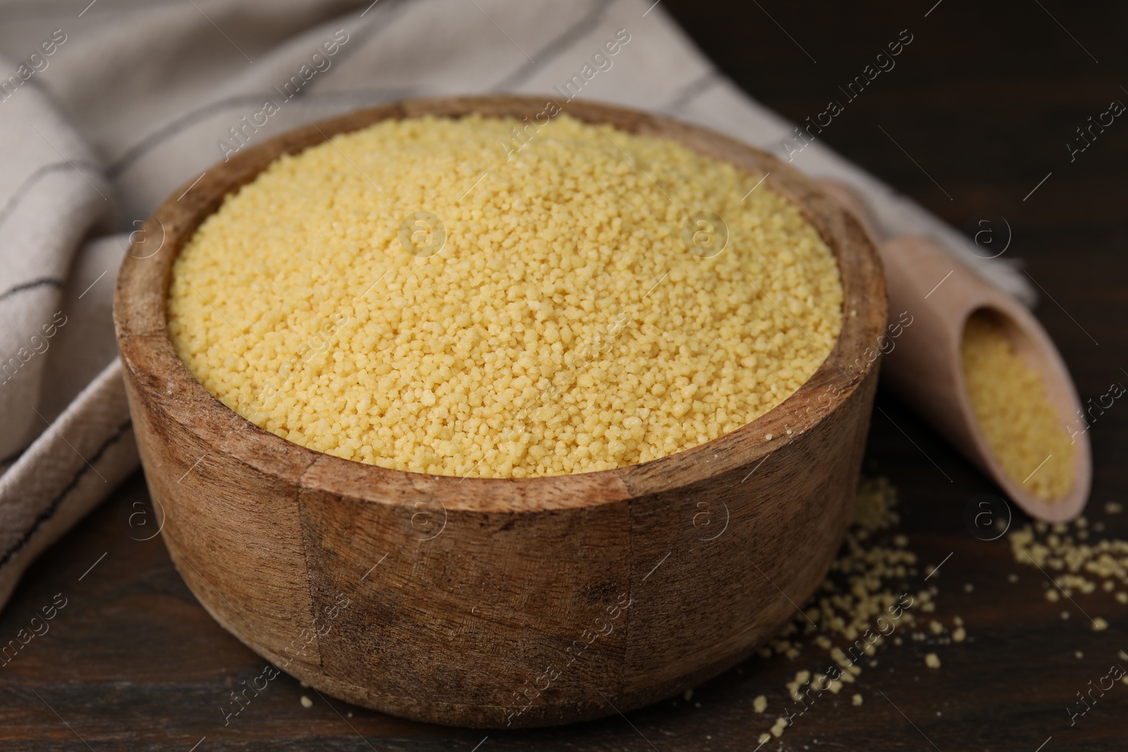 Photo of Raw couscous in bowl on wooden table, closeup