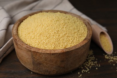 Raw couscous in bowl on wooden table, closeup