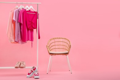 Rack with different stylish women`s clothes, sneakers and armchair on pink background, space for text
